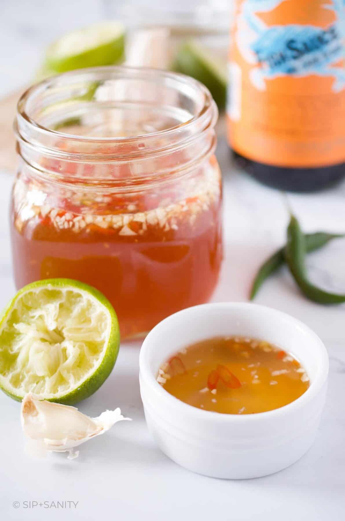 Jar of nuoc mam next to a small dish, half a lime and garlic.